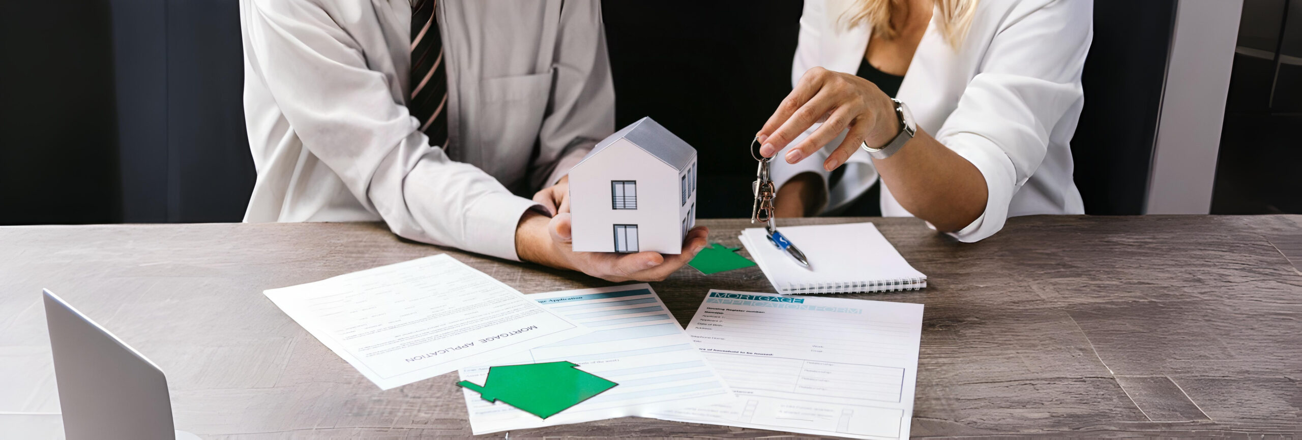 Realtor handing house keys to new owner over mortgage documents and a model house